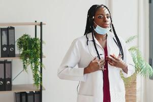 medicine, profession and healthcare concept - african american female doctor or scientist in protective facial mask in clinic. photo