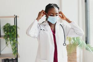 medicine, profession and healthcare concept - african american female doctor or scientist in protective facial mask in clinic. photo