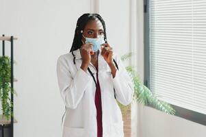 medicine, profession and healthcare concept - african american female doctor or scientist in protective facial mask in clinic. photo