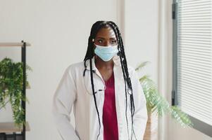 medicine, profession and healthcare concept - african american female doctor or scientist in protective facial mask in clinic. photo