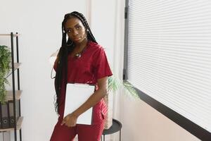 Portrait Of Smiling Female Doctor Wearing Scrubs In Hospital Corridor Holding Digital Tablet. photo