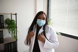 medicine, profession and healthcare concept - african american female doctor or scientist in protective facial mask in clinic. photo