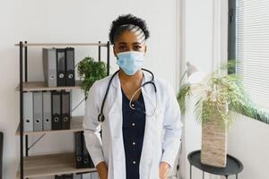 medicine, profession and healthcare concept - african american female doctor or scientist in protective facial mask in clinic. photo