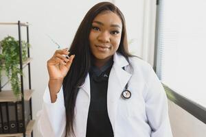 healthcare and medical concept - african doctor holding syringe with injection. photo