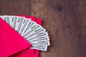 Close-up of red envelopes packet with US banknotes or Ang Pao prepare for giving to children in Chinese New Year. Wooden table background and space for text. Festival concept photo