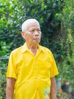 Portrait of a senior man wearing a yellow shirt looking up and worried while standing in a garden. Concept of aged people and healthcare photo