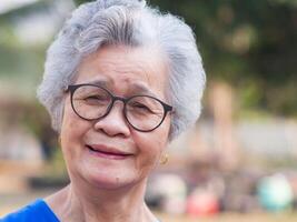 Portrait of a happy senior woman with short gray hair, wearing glasses, smiling and looking at the camera while standing outdoors. Space for text Concept of aged people and healthcare photo