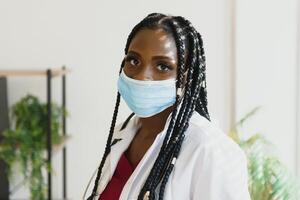 medicine, profession and healthcare concept - african american female doctor or scientist in protective facial mask in clinic. photo