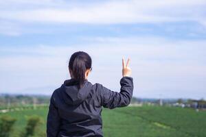 Back view of a woman hand showing v-sign while standing looking at the tea plantation. Space for text. Relaxation concept photo