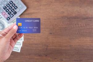 Close-up of hand holding a credit card with money US dollars background and a calculator placed on a wooden table. Space for text. Concept of business, e-commerce, and payment photo