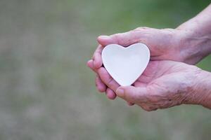 de cerca Disparo de un en forma de corazon blanco cerámico en el palma de un mayor mujer. San Valentín día. espacio para texto. concepto de Envejecido personas y cuidado de la salud foto