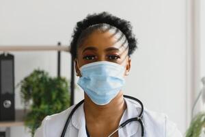 medicine, profession and healthcare concept - african american female doctor or scientist in protective facial mask in clinic. photo