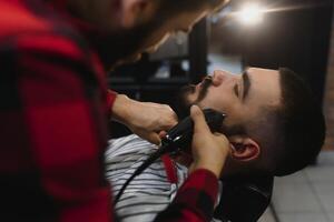 joven barbado hombre consiguiendo barba Corte de pelo por Barbero. barbería tema. foto