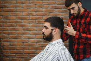 hermoso barbado hombre es sonriente mientras teniendo su pelo cortar por peluquero a el peluquería. foto