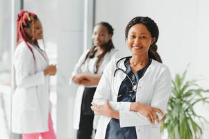 health care, profession, people and medicine concept - happy african american female doctor or nurse over group of medics meeting at hospital. photo