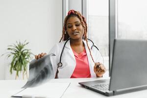 medicine, online service and healthcare concept - happy smiling african american female doctor or nurse with headset and laptop having conference or call at hospital. photo