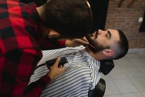 Young Bearded Man Getting Beard Haircut By Barber. Barbershop Theme. photo