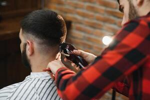 Handsome bearded man is smiling while having his hair cut by hairdresser at the barbershop. photo