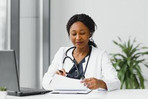 africano americano mujer médico trabajando a su oficina en línea utilizando portátil informacion dispositivo. telemedicina servicios. primario cuidado consultas, psicoterapia, emergencia servicios foto