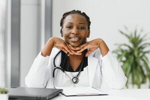 de cerca retrato de amigable, sonriente confidente hembra cuidado de la salud profesional con laboratorio abrigo, estetoscopio, brazos cruzado. aislado hospital clínica antecedentes. hora para un oficina visita. foto