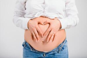 embarazada mujer participación su manos en un corazón forma en su bebé bulto. embarazada barriga con dedos corazón símbolo. maternidad concepto. bebé ducha foto