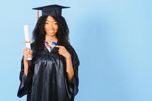 African-American beautiful woman in a black robe and hat, on a blue isolated background smiles. photo