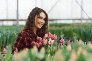 Beautiful young smiling girl, worker with flowers in greenhouse. Concept work in the greenhouse, flowers, tulips, box with flowers. Copy space. photo