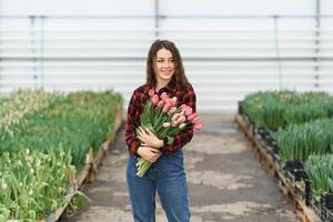 Beautiful young smiling girl, worker with flowers in greenhouse. Concept work in the greenhouse, flowers. photo