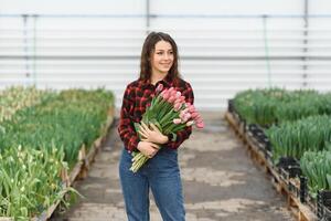 Beautiful young smiling girl, worker with flowers in greenhouse. Concept work in the greenhouse, flowers, tulips, box with flowers. Copy space. photo