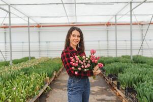 Beautiful young smiling girl, worker with flowers in greenhouse. Concept work in the greenhouse, flowers, tulips, box with flowers. Copy space. photo