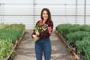 Beautiful young smiling girl, worker with flowers in greenhouse. Concept work in the greenhouse, flowers. photo