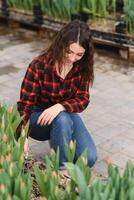 hermosa joven sonriente chica, trabajador con flores en invernadero. concepto trabajo en el invernadero, flores, tulipanes, caja con flores Copiar espacio. foto