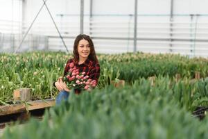 Beautiful young smiling girl, worker with flowers in greenhouse. Concept work in the greenhouse, flowers. photo