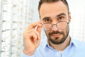 Young man choosing spectacles at optic shop photo