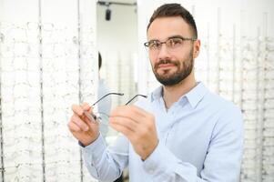 Healthcare, Eyesight And Vision Concept. Happy man choosing glasses at optics store, selective focus photo