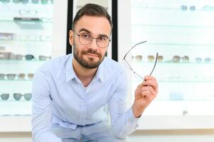 joven hombre elegir gafas a óptico tienda foto