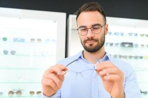 joven hombre elegir gafas a óptico tienda foto