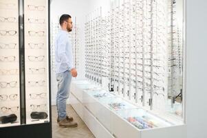 Young man choosing spectacles at optic shop photo