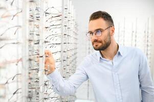 joven hombre elegir gafas a óptico tienda foto