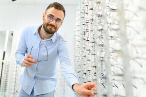 Healthcare, Eyesight And Vision Concept. Happy man choosing glasses at optics store, selective focus photo