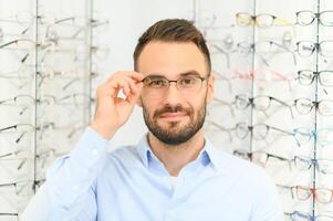 joven hombre elegir gafas a óptico tienda foto