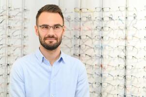 Healthcare, Eyesight And Vision Concept. Happy man choosing glasses at optics store, selective focus photo