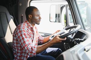 Professional african american truck driver in casual clothes driving truck vehicle going for a long transportation route. photo