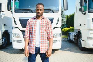 Front view. Young african truck driver is with his vehicle at daytime. photo