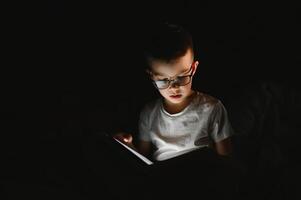 Reading book and using flashlight. Young boy in casual clothes lying down near tent at evening time photo