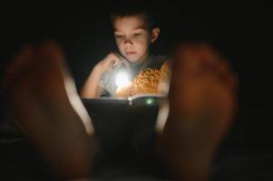 Portrait of cute little boy reading in bed with flashlight in dark room, enjoying fairytales. photo