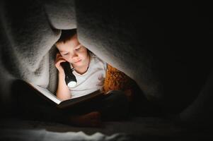 Reading book and using flashlight. Young boy in casual clothes lying down near tent at evening time photo