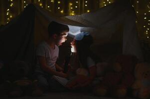 children boy and girl playing and frighten each other with flashlight in tent at night photo