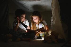 happy family children reading a book with a flashlight in a tent at home photo