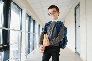 Happy smiling boy in glasses is going to school for the first time. Child with school bag and book in his hand. Kid indoors of the class room . Back to school. photo